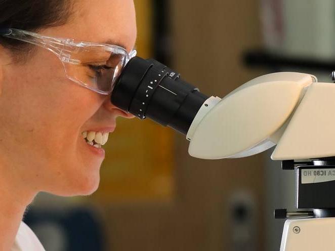Woman with safety goggles on looking through a biology microscope